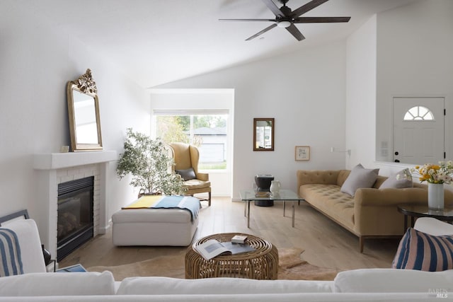 living area with high vaulted ceiling, a ceiling fan, a brick fireplace, and wood finished floors