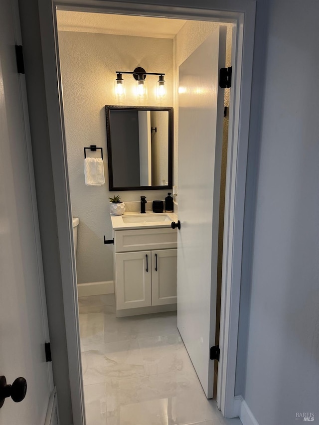 half bath featuring baseboards, marble finish floor, vanity, and toilet
