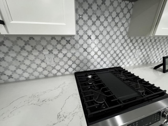 room details with white cabinets, stovetop, tasteful backsplash, and light stone counters