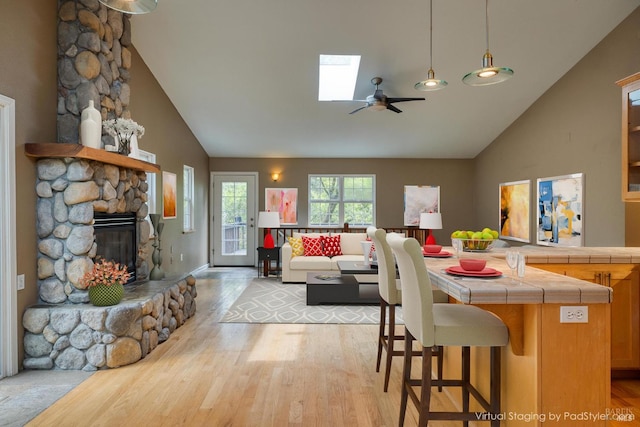 16589 Glenda Dr, Guerneville, CA 95446 - dining room with light wood-style flooring, high vaulted ceiling, a ceiling fan, a stone fireplace, and a skylight