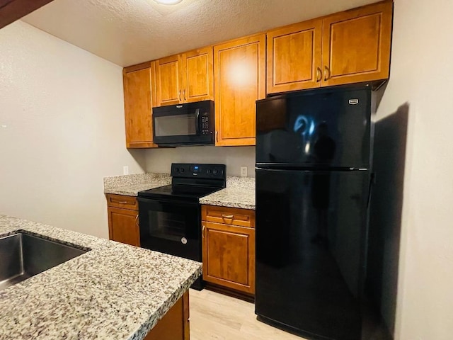 kitchen featuring light wood finished floors, light stone countertops, brown cabinets, and black appliances