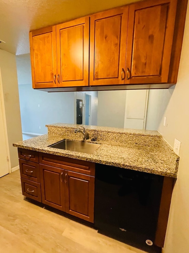 kitchen with brown cabinetry, light stone countertops, light wood finished floors, and a sink