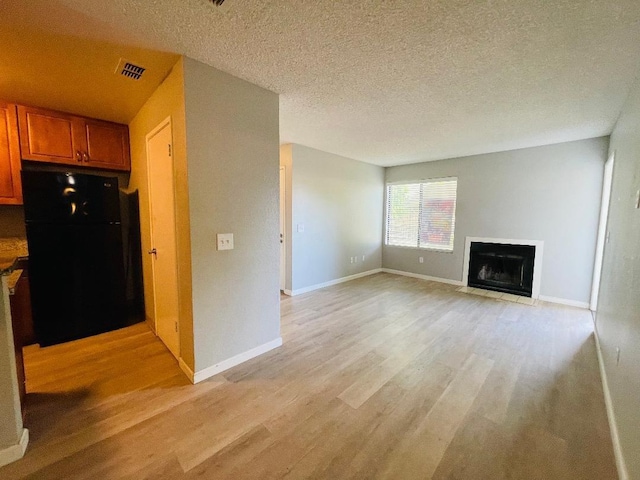 unfurnished living room featuring a textured ceiling, a fireplace with flush hearth, light wood-style flooring, baseboards, and visible vents