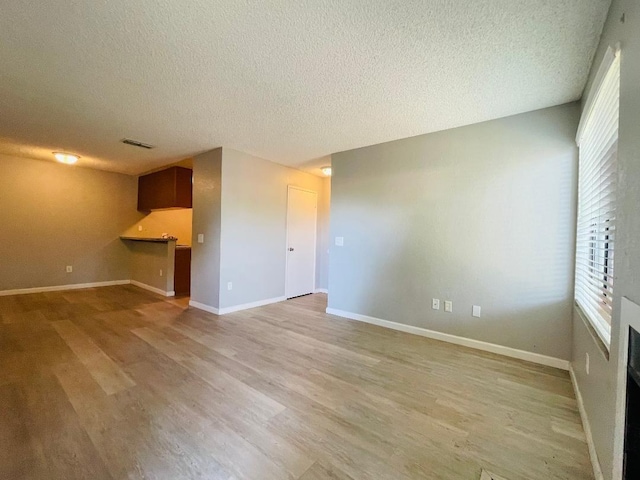 unfurnished living room featuring light wood finished floors, baseboards, visible vents, and a textured ceiling