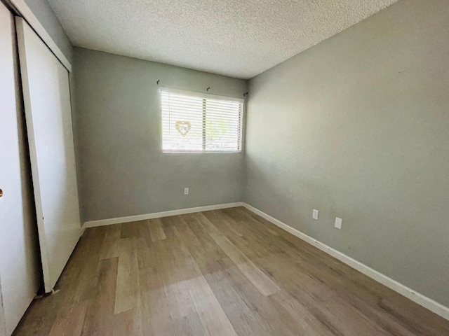 unfurnished bedroom with baseboards, wood finished floors, a textured ceiling, and a closet