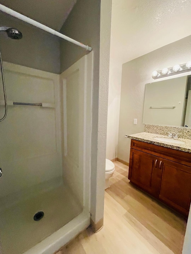 full bath with toilet, wood finished floors, vanity, and a stall shower