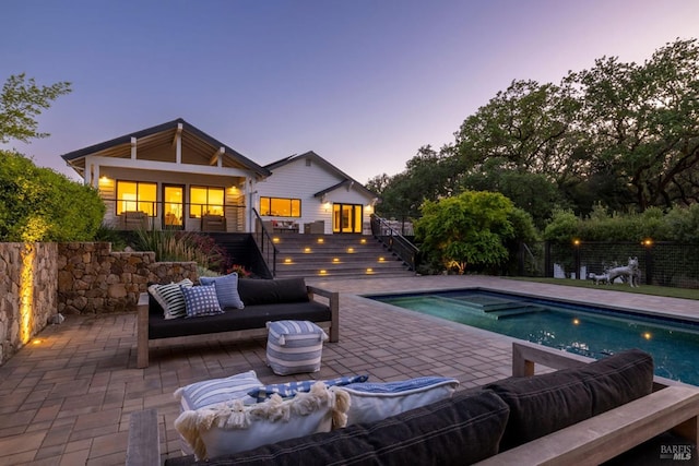 back of house at dusk featuring outdoor lounge area, a fenced in pool, a patio, and stairs