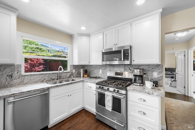 kitchen with white cabinets, light stone countertops, stainless steel appliances, and a sink