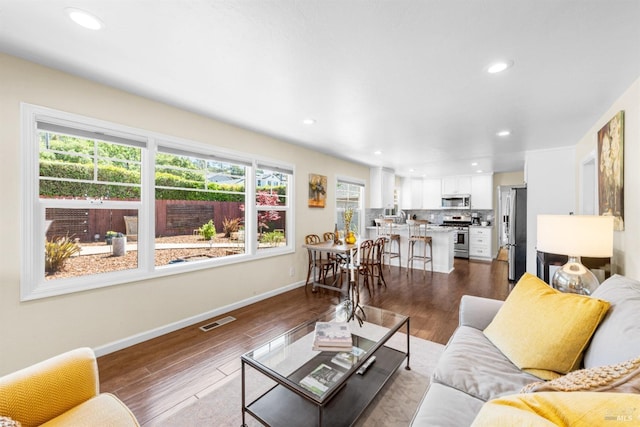 living area featuring dark wood-type flooring, plenty of natural light, visible vents, and baseboards