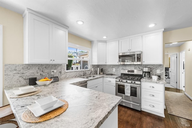 kitchen with white cabinets, a peninsula, stainless steel appliances, and a sink