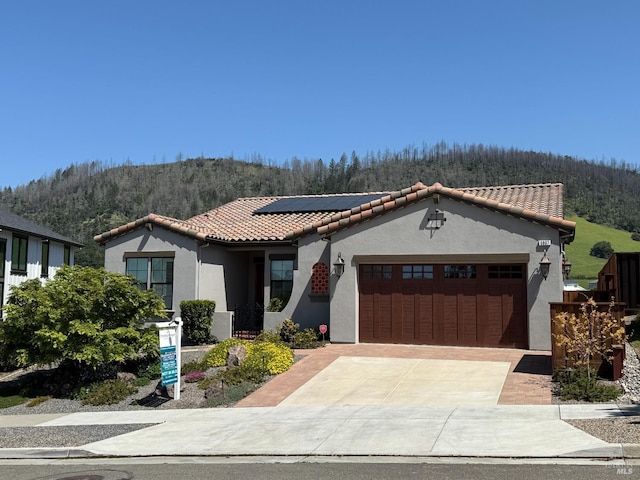 mediterranean / spanish home featuring stucco siding, a tile roof, solar panels, and a garage