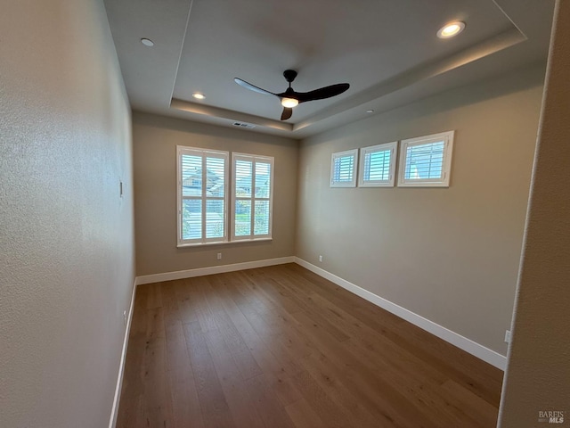spare room featuring hardwood / wood-style flooring, ceiling fan, a tray ceiling, baseboards, and recessed lighting