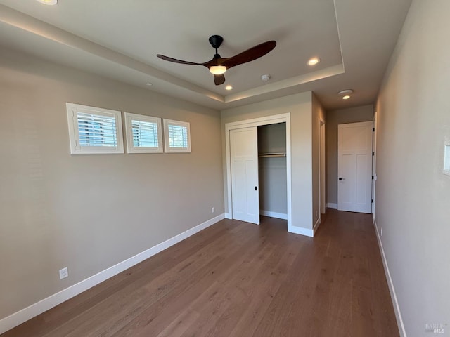 unfurnished bedroom featuring baseboards, wood finished floors, and a tray ceiling
