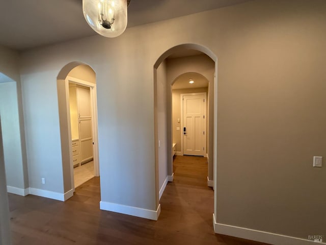 hallway featuring dark wood-style floors, baseboards, and arched walkways