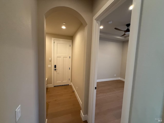 hallway featuring baseboards, recessed lighting, arched walkways, and wood finished floors