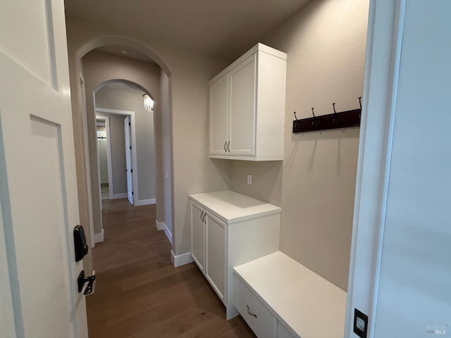 mudroom with arched walkways, wood finished floors, and baseboards