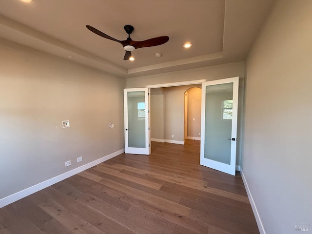 unfurnished bedroom with arched walkways, baseboards, a raised ceiling, and dark wood-type flooring