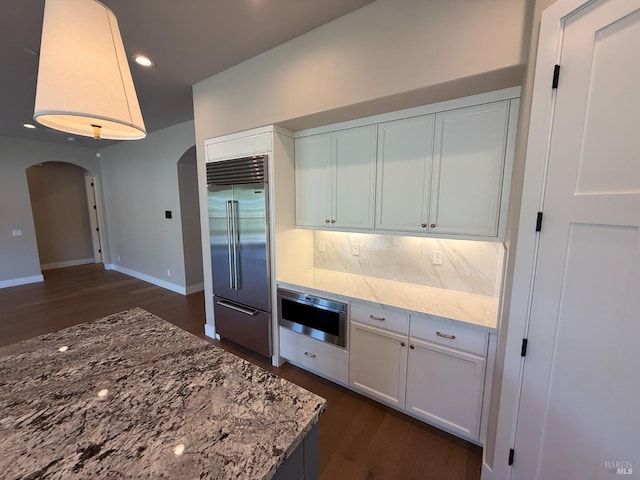 kitchen with dark wood-type flooring, built in fridge, wall oven, and arched walkways