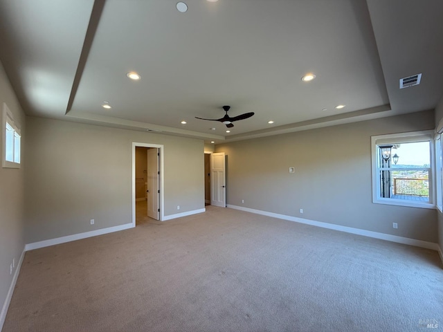 unfurnished room featuring a raised ceiling, a healthy amount of sunlight, visible vents, and light carpet