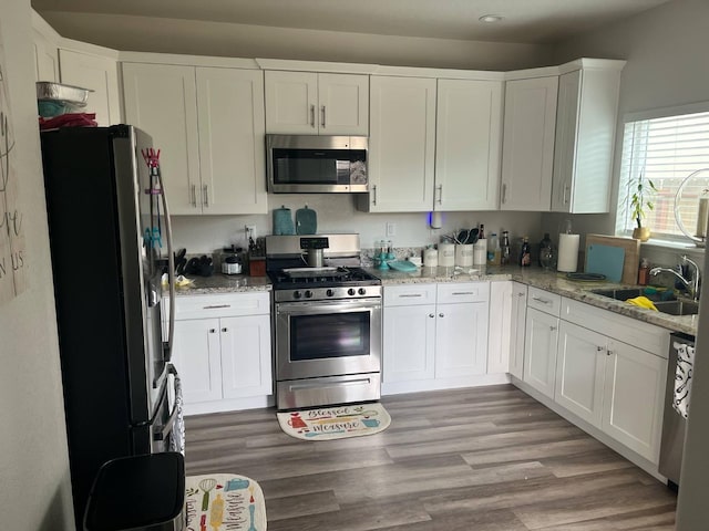 kitchen with light stone countertops, light wood-style floors, white cabinets, a sink, and appliances with stainless steel finishes