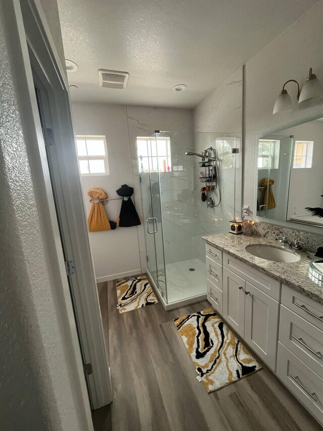 bathroom featuring a textured ceiling, visible vents, a shower stall, wood finished floors, and vanity