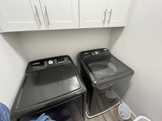 washroom featuring wood finished floors, cabinet space, and washing machine and clothes dryer