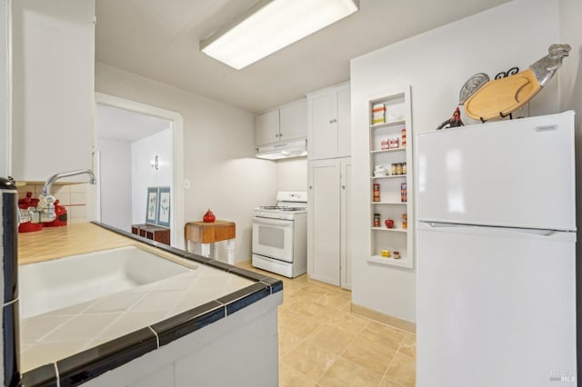 kitchen featuring white cabinets, under cabinet range hood, tile countertops, a sink, and white appliances