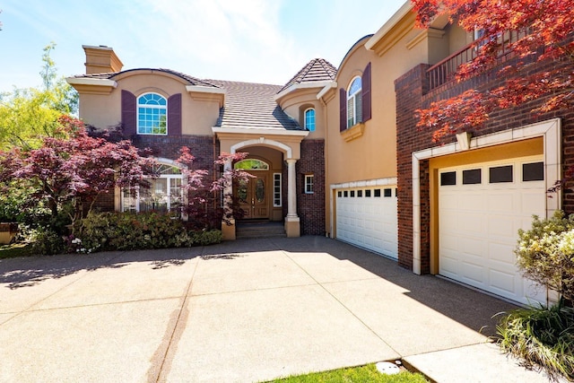 mediterranean / spanish-style house featuring driveway, a chimney, a garage, brick siding, and stucco siding