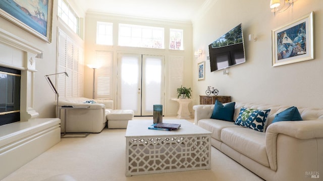 living room featuring a glass covered fireplace, carpet, a towering ceiling, and ornamental molding