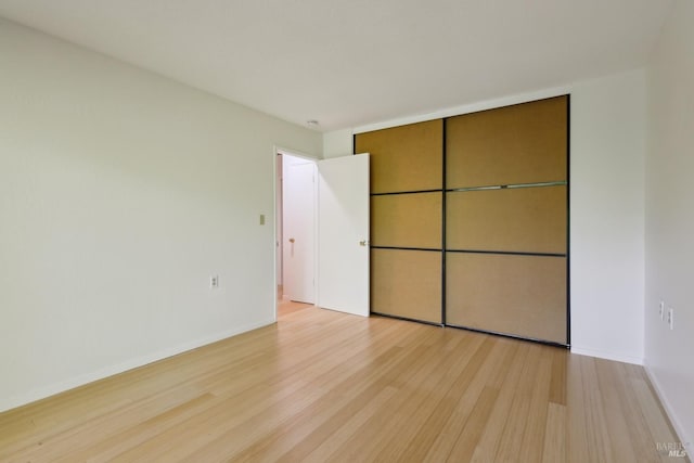 unfurnished bedroom featuring light wood-style flooring, baseboards, and a closet