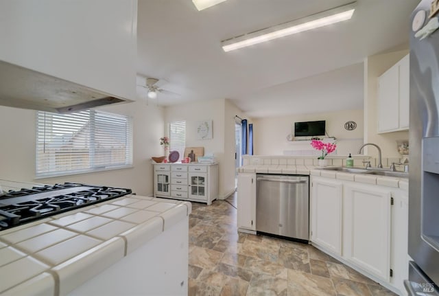 kitchen with tile counters, stone finish floor, a ceiling fan, a sink, and appliances with stainless steel finishes