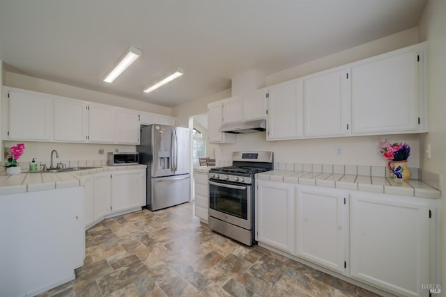 kitchen with stainless steel appliances, a sink, white cabinetry, tile counters, and under cabinet range hood