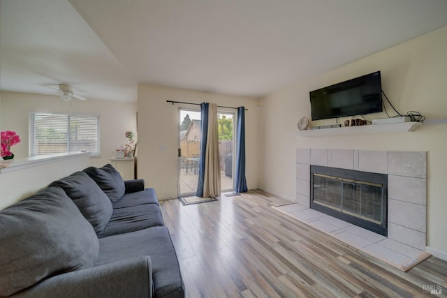 living room with baseboards, a tiled fireplace, wood finished floors, and a ceiling fan