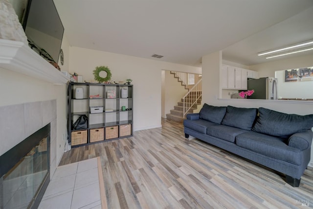 living room with baseboards, visible vents, light wood-style floors, stairs, and a fireplace