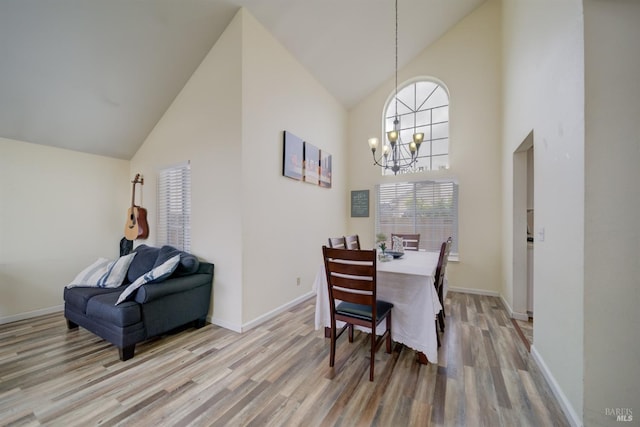dining space featuring a chandelier, light wood-style floors, baseboards, and high vaulted ceiling