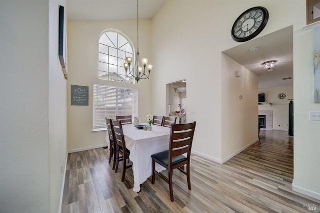 dining space featuring wood finished floors, baseboards, an inviting chandelier, a tiled fireplace, and a high ceiling