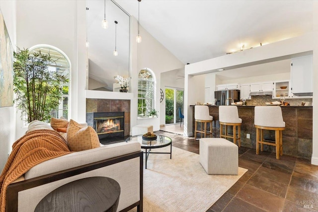 living room featuring high vaulted ceiling, stone tile floors, and a tiled fireplace