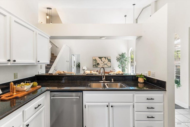 kitchen with stainless steel dishwasher, dark stone countertops, a sink, light tile patterned flooring, and white cabinetry