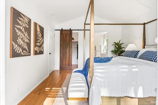 bedroom featuring a barn door, baseboards, a spacious closet, lofted ceiling, and wood finished floors