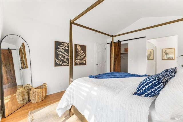 bedroom featuring a barn door, vaulted ceiling, and wood finished floors