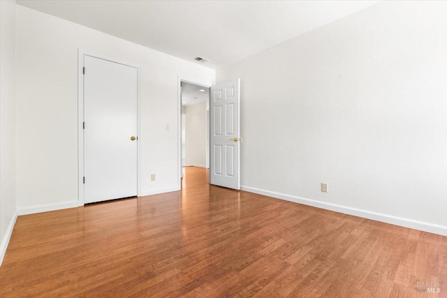 spare room featuring wood finished floors, visible vents, and baseboards
