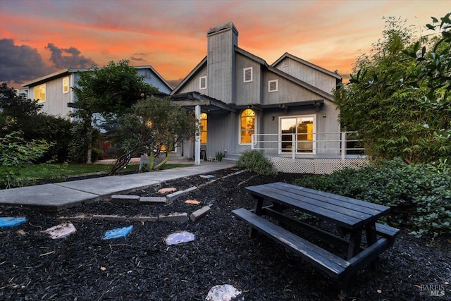 back of property at dusk featuring a porch and a chimney