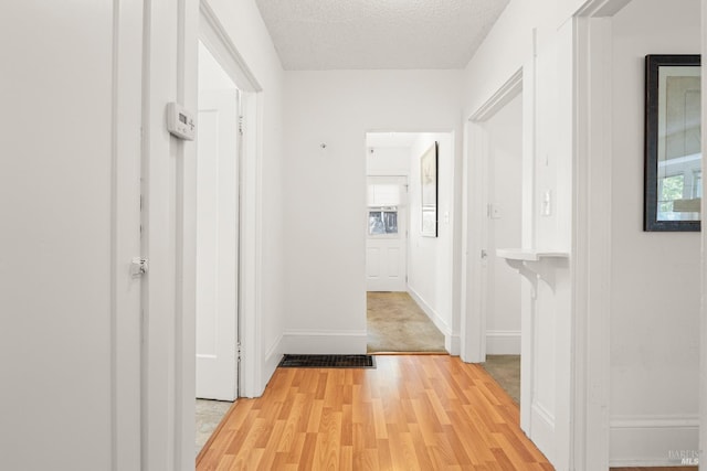hallway featuring light wood-style floors, a textured ceiling, and baseboards