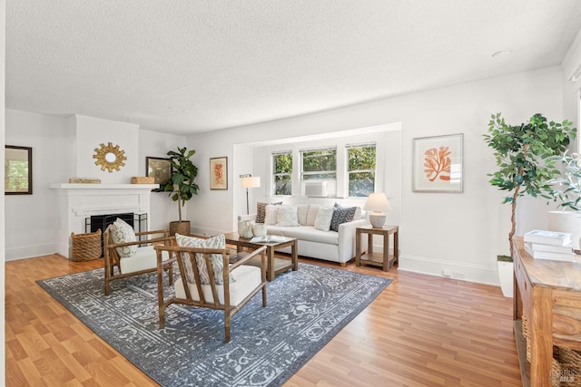 living room featuring a fireplace, baseboards, a textured ceiling, and light wood-type flooring