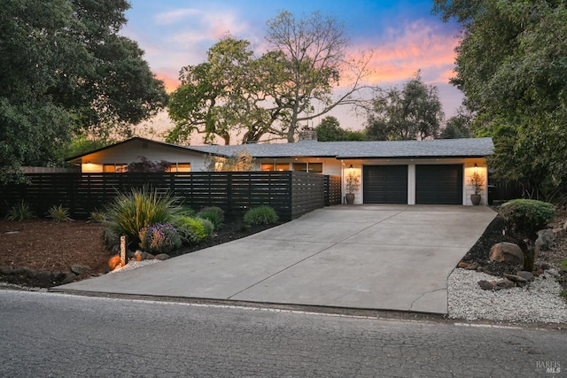 mid-century home with an attached garage, stone siding, a fenced front yard, and concrete driveway