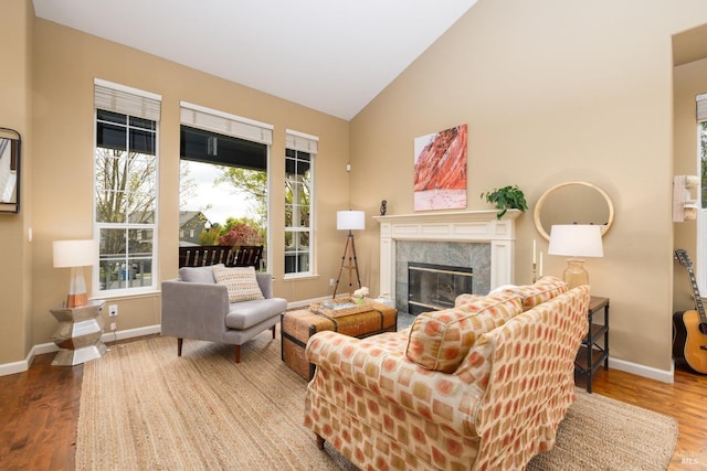living room with wood finished floors, baseboards, high vaulted ceiling, and a high end fireplace