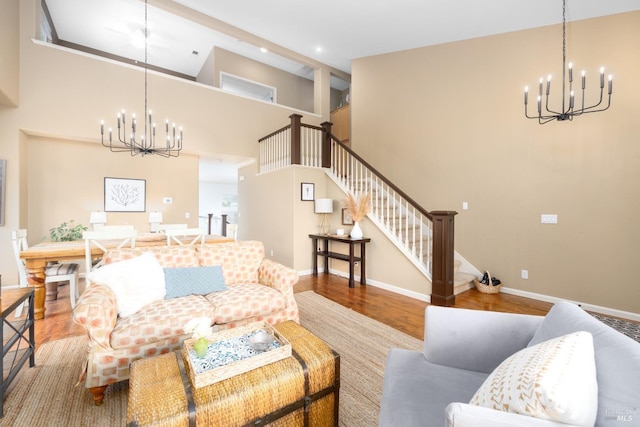 living room featuring stairway, a towering ceiling, wood finished floors, baseboards, and a chandelier