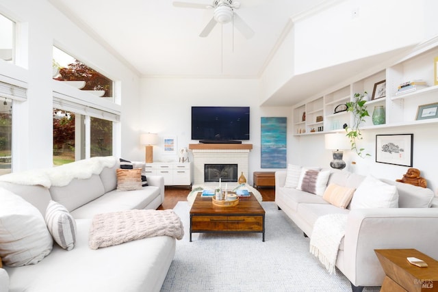 living area with a glass covered fireplace, built in shelves, a ceiling fan, wood finished floors, and crown molding