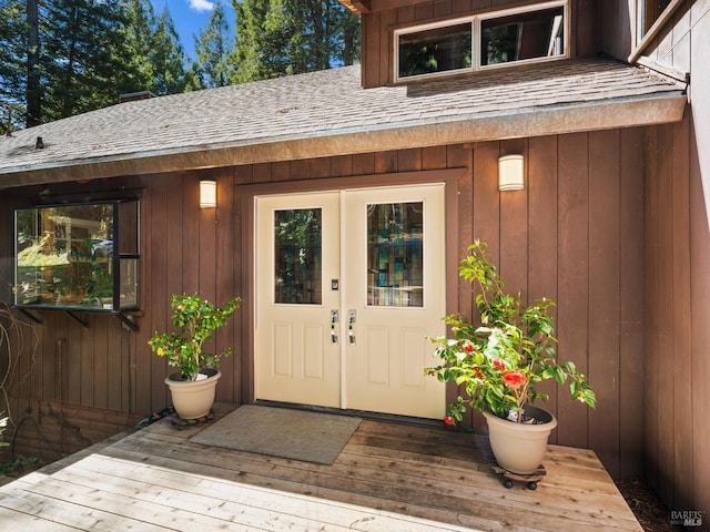 entrance to property with board and batten siding, roof with shingles, and a deck