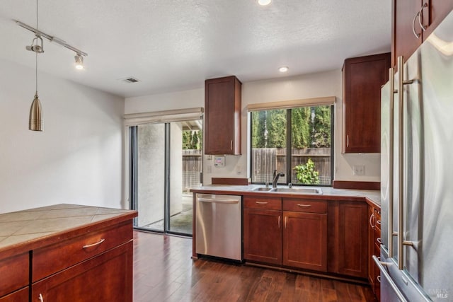 kitchen with hanging light fixtures, a sink, stainless steel appliances, tile countertops, and dark wood-type flooring